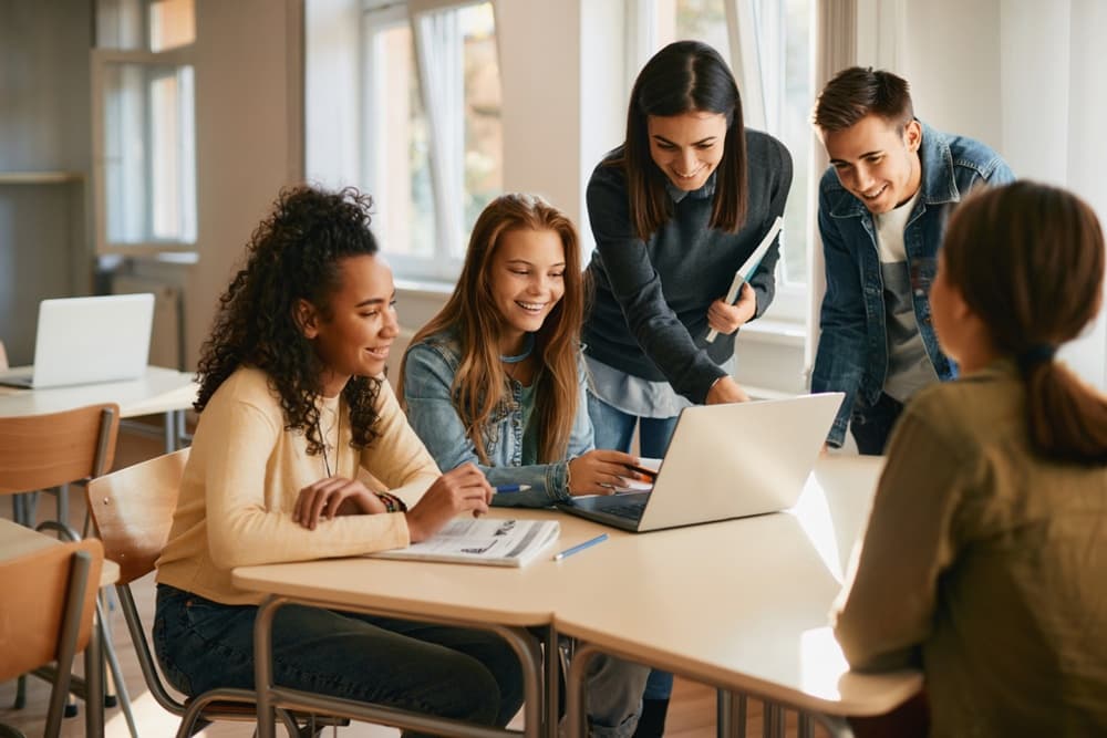 Students working through a task together around a laptop in a classroom